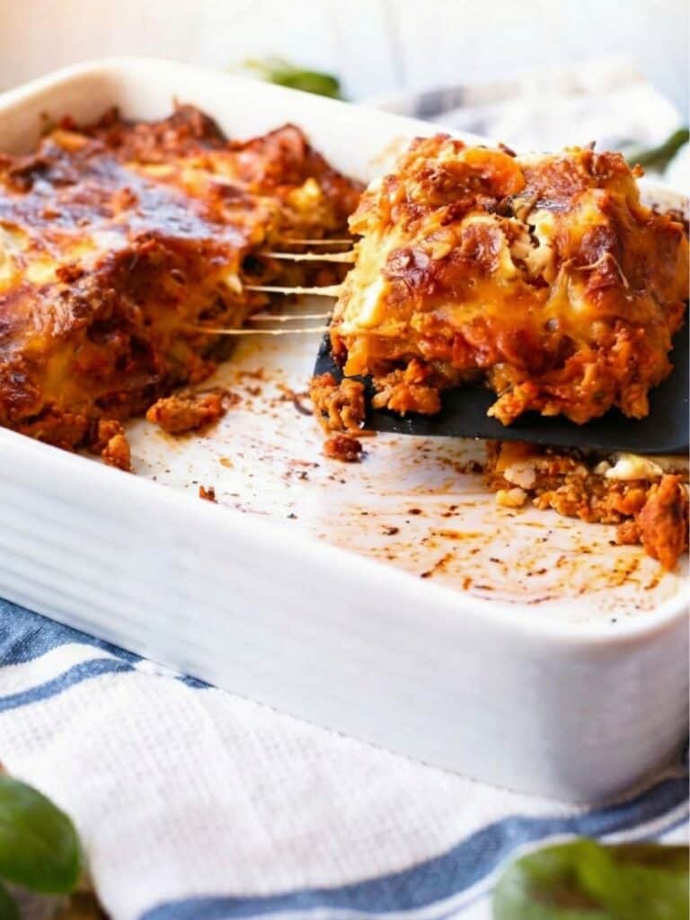 a side view of Chicken Pumpkin Ricotta Lasagna with half of the lasagna taken out and a large slice on a plastic spoon being taken out.