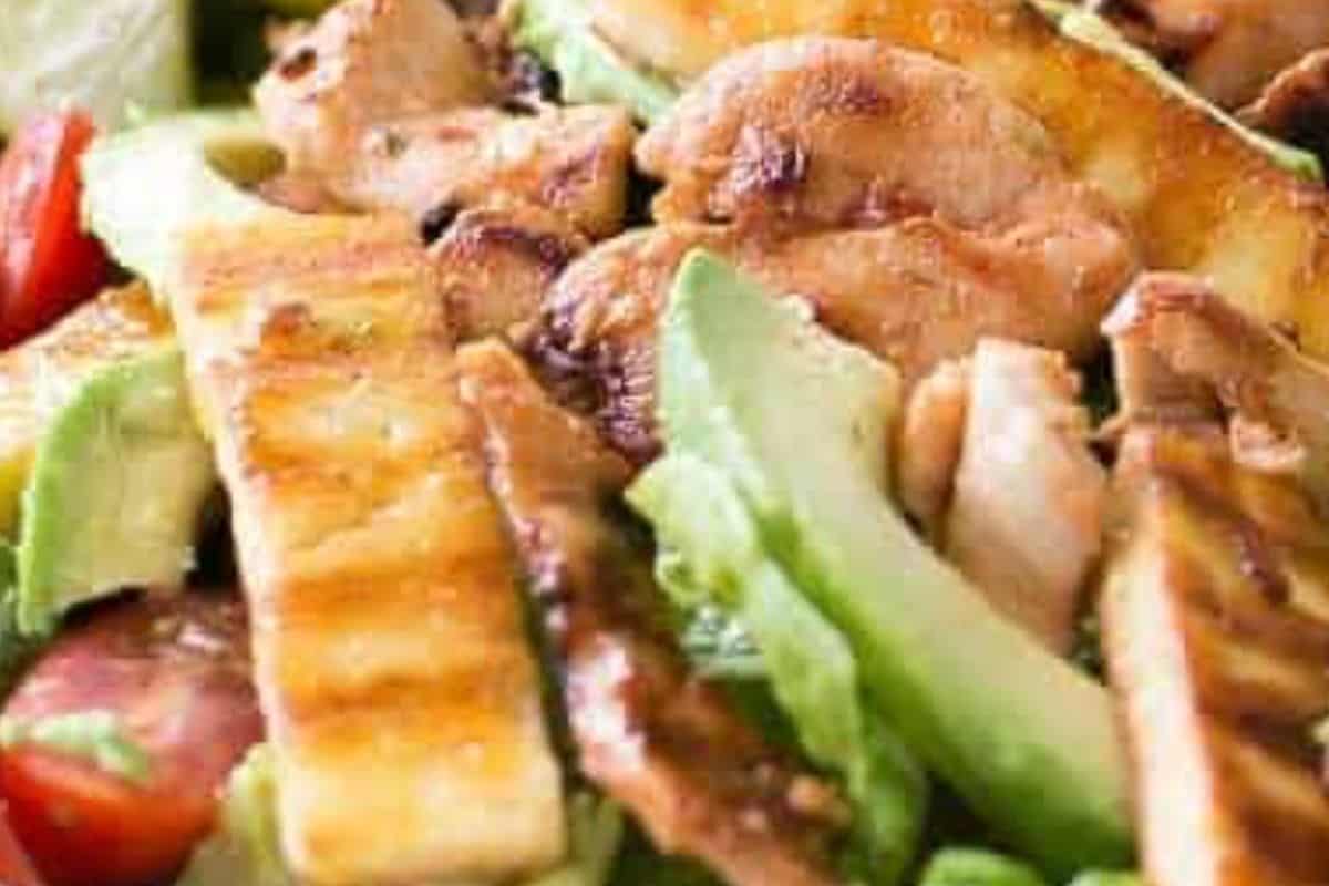 combine salad leaves, tomatoes, and avocado on plates, top with the warm chicken and halloumi, drizzle with dressing, and serve with lime wedges