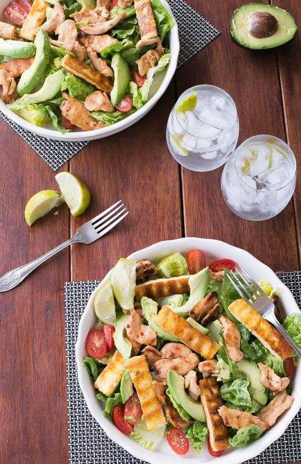 2 bowls filled with Sweet Chilli Chicken, Haloumi and Avocado Salad with Lime Dressing and 2 glass with some drink