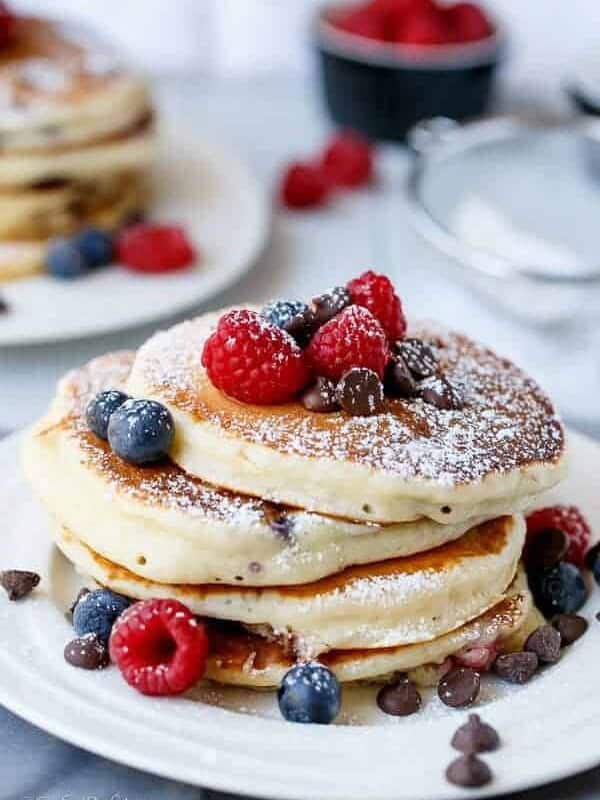 Fluffy Greek Yoghurt and Mixed Berry Choc Chip Pancakes being stack on each other with some fresh berries on top