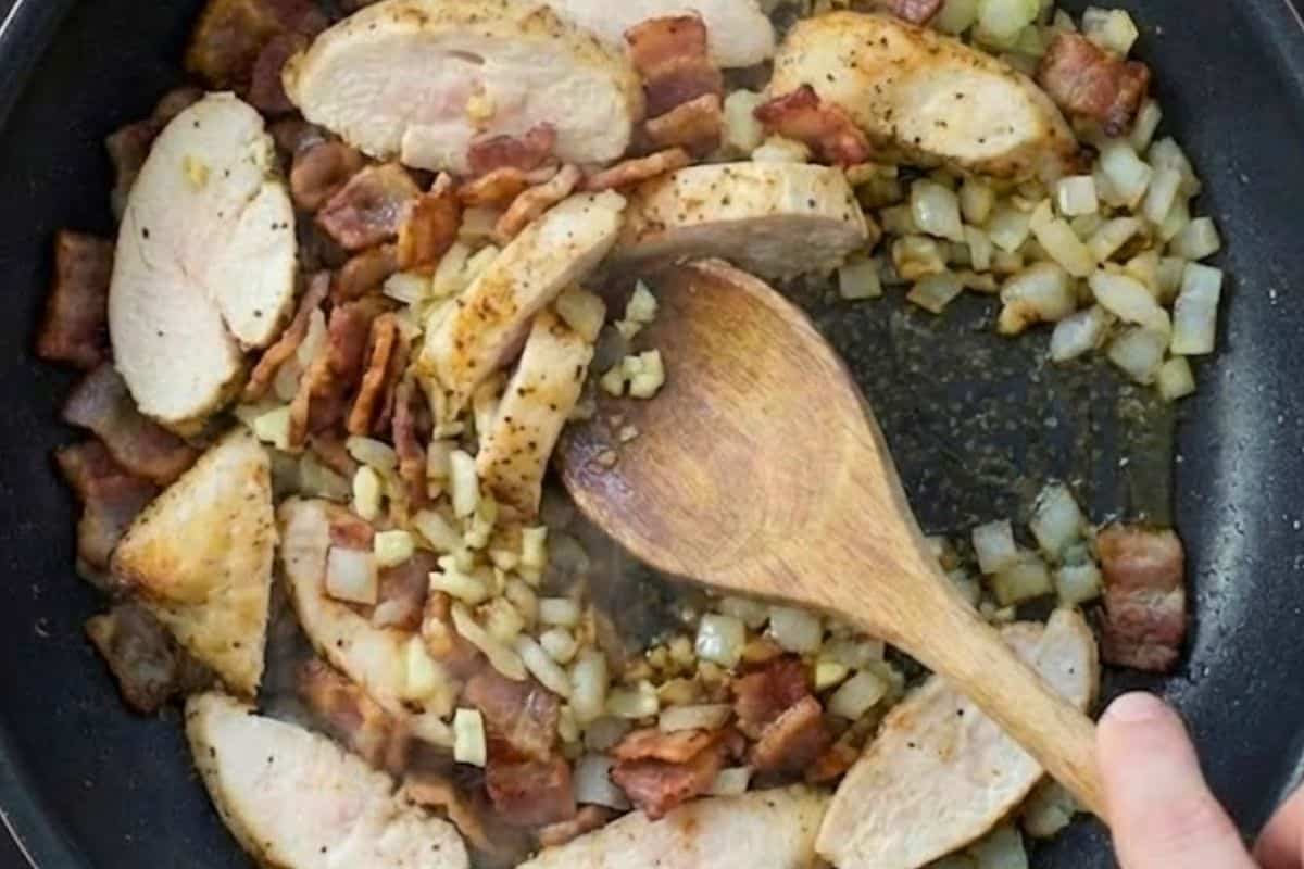 Heat a non stick frying pan over medium high heat and cook the onion and bacon until the bacon is crisp, about 6 minutes, then add the garlic and chicken and cook until the chicken is cooked through.