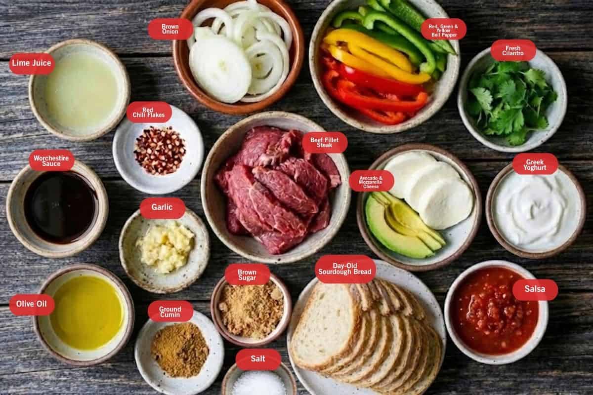 Flat lay photo of ingredient shot of lime juice, brown onion, red, green and yellow bell pepper, fresh cilantro, greek yogurt, salsa, day old sour dough bread, salt, brown sugar, garlic, beef fillet steak, olive oil, worchestire sauce, lime juice, red chili flakes, garlic, ground cumin