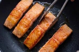 Moving cooked salmon on a pan with hot oil