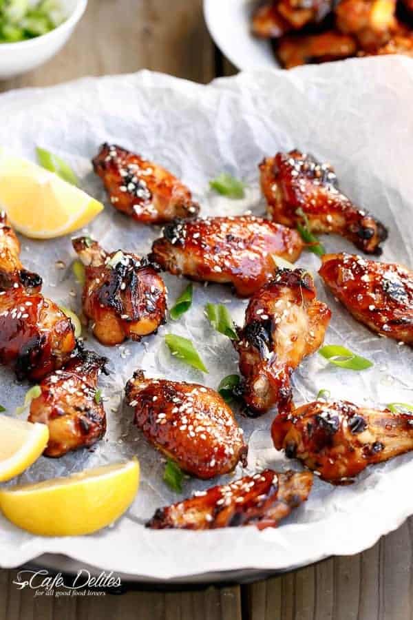 Sticky Honey Sesame Chicken Wings with lemon wedges on a baking tray