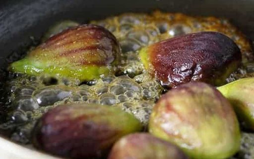 half-cut figs sitting in a pan with melted butter and honey cut face down, sizzling and caramelizing. You can see the bubbles from the butter and honey mix.