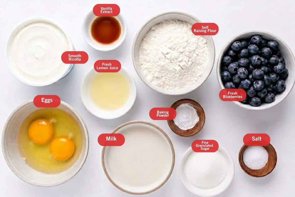 Flat lay photo of ingredient shot of smooth ricotta, vanilla extract, self raising flour, fresh blueberries, fresh lemon juice, milk, baking powder, fine granulated sugar, salt, eggs