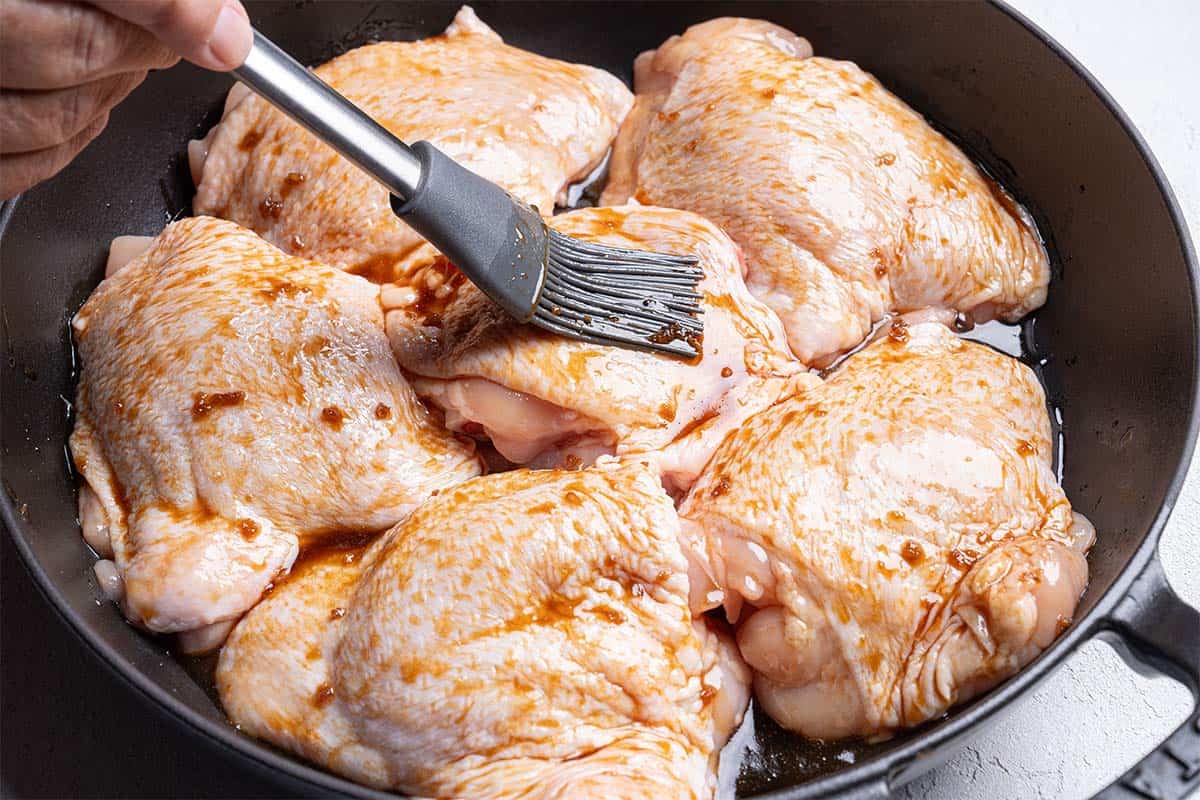 chicken being coated with a brush with sauce