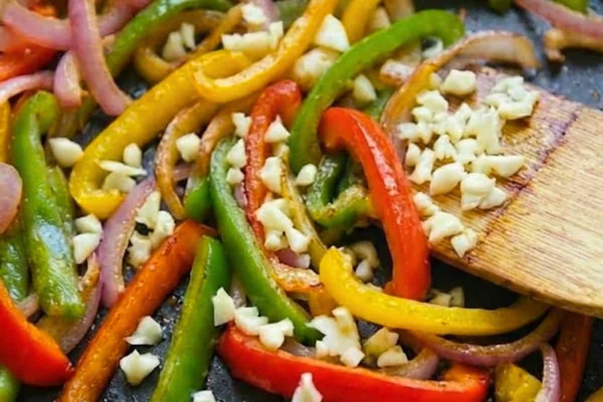 While the potatoes cook, heat olive oil in a skillet over medium-high heat. Add sliced onion and cook until soft, then toss in the garlic and bell peppers until fragrant.
