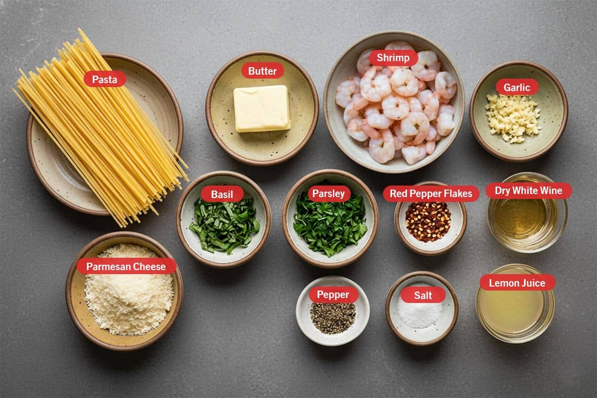 Top shot of ingredients: pasta, butter, shrimp, garlic, parmesan cheese, basil, parsley, red pepper flakes, dry white wine, pepper, salt, and lemon juice.