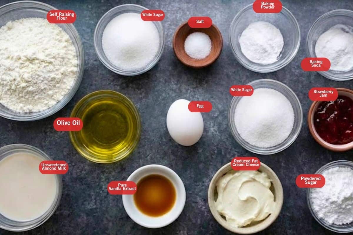 Flat lay photo of ingredient shot of self raising flour, white sugar, salt, baking powder, baking soda, strawberry jam, powdered sugar, reduced fat cream cheese, egg, pure vanilla extract, unsweetened almond milk, olive oil.