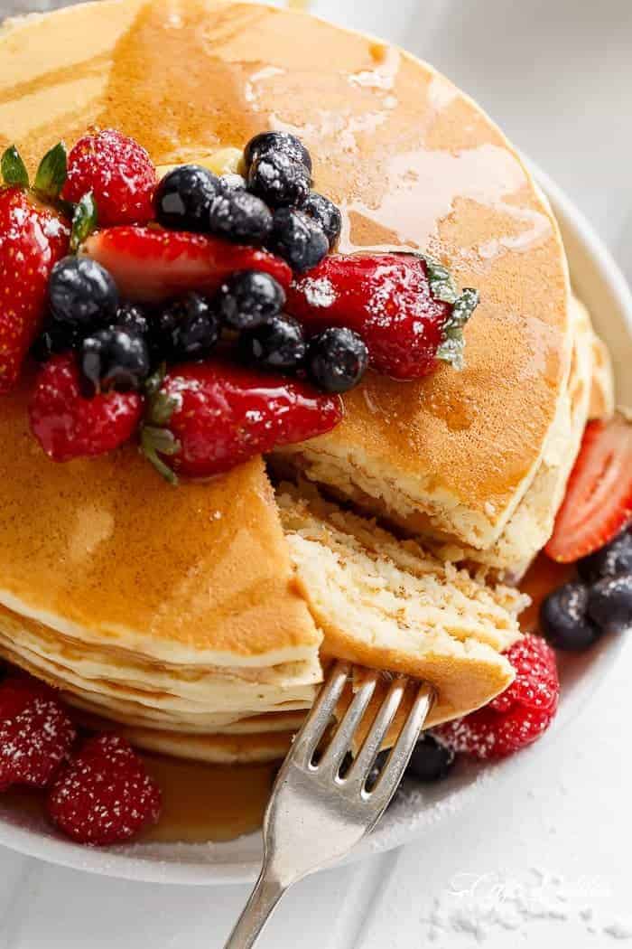 Top view of a finished pancake stack garnished with mixed berries, being sliced open by a fork, and ready to enjoy.