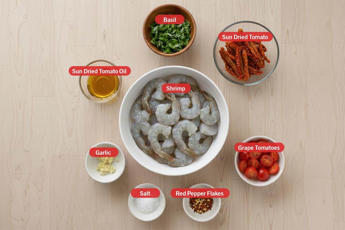 Top shot of ingredients: basil, sun dried tomatoes, grape tomatoes, red pepper flakes, salt, garlic, sun dried tomato oil, and shrimp.