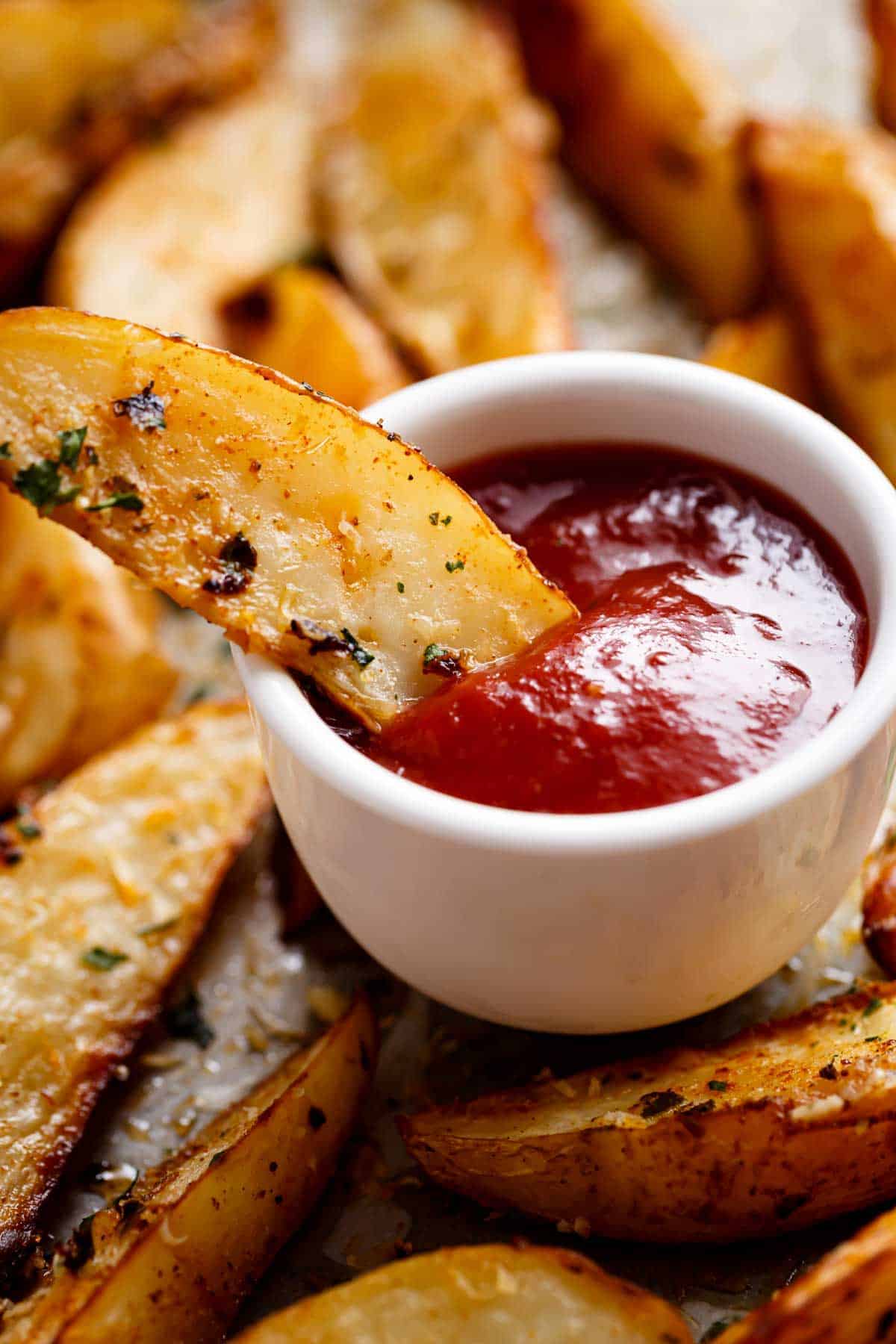 Baked potato wedges served with tomato ketchup in a bowl.