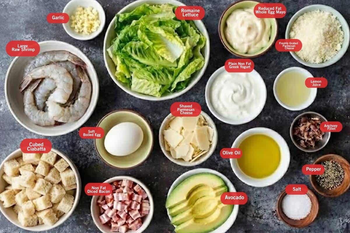 Flat lay photo of cubed ciabatta, large raw shrimp, lemon juice, garlic, salt, pepper, non fat diced bacon, soft boiled egg, romaine lettuce, avocado, shaved parmesan cheese, non far greek yogurt, reduced fat whole egg mayo, olive oil, freshly grated parmesan cheese