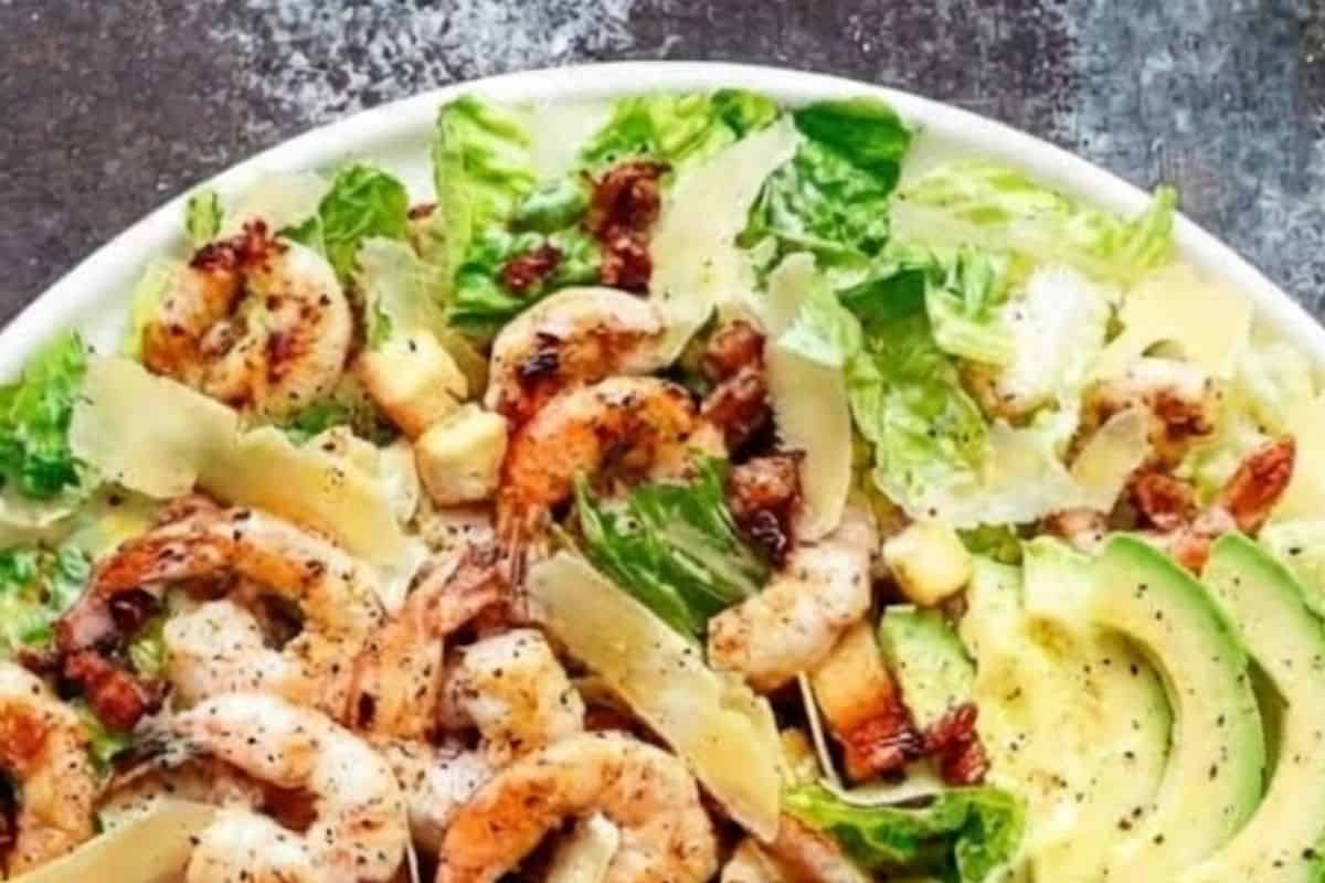 Place the washed and dried romaine lettuce into a large salad bowl. Add the warm shrimp, crispy bacon, avocado slices, shaved Parmesan, and toasted croutons.
