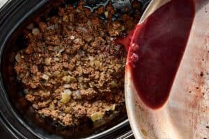 Deglazed wine mixture being poured into slow cooker with beef