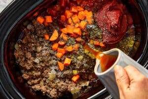 Ingredients including tomatoes, carrots, and seasoning added to slow cooker