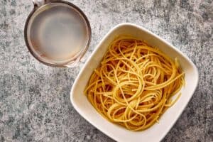 Bolognese sauce and pasta water being added to cooked spaghetti