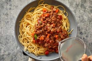 Bolognese sauce and pasta water being added to cooked spaghetti