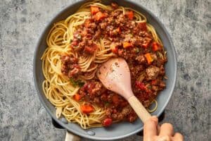 Spaghetti being tossed with bolognese sauce until coated