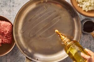Olive oil being added to a large skillet for spaghetti bolognese