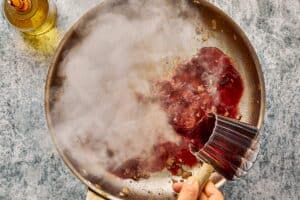 Deglazed wine mixture being poured into slow cooker with beef