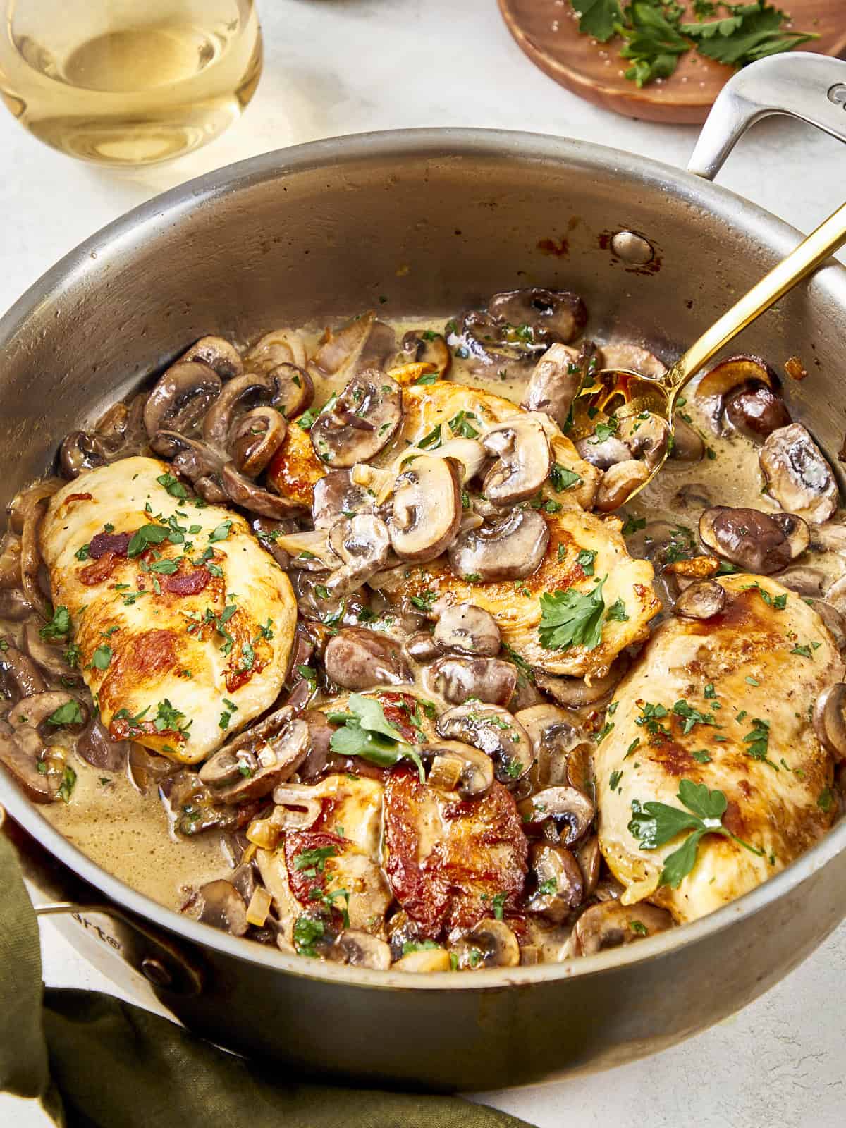 Golden seared chicken breasts simmered in a creamy champagne mushroom sauce, garnished with fresh parsley in a stainless steel skillet.