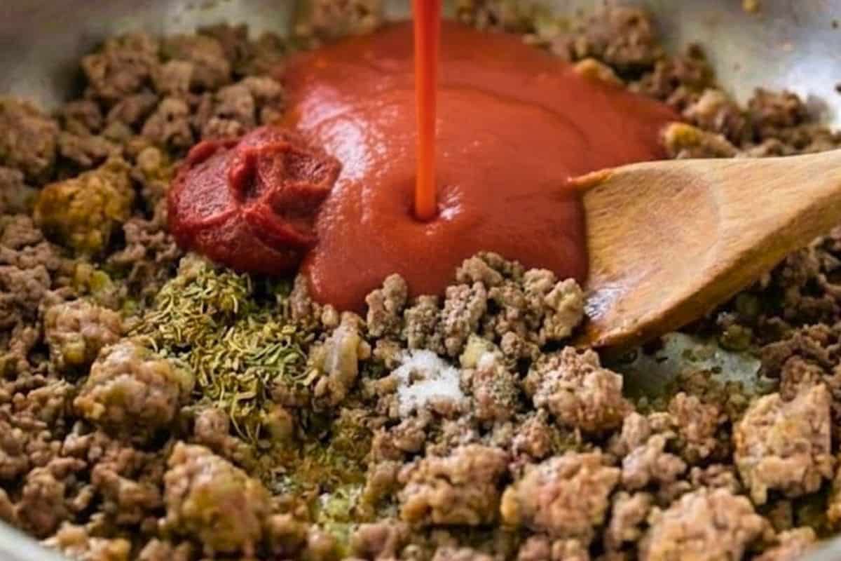Stir in three quarters of the tomato puree, tomato paste, bouillon, salt, pepper, oregano, and basil