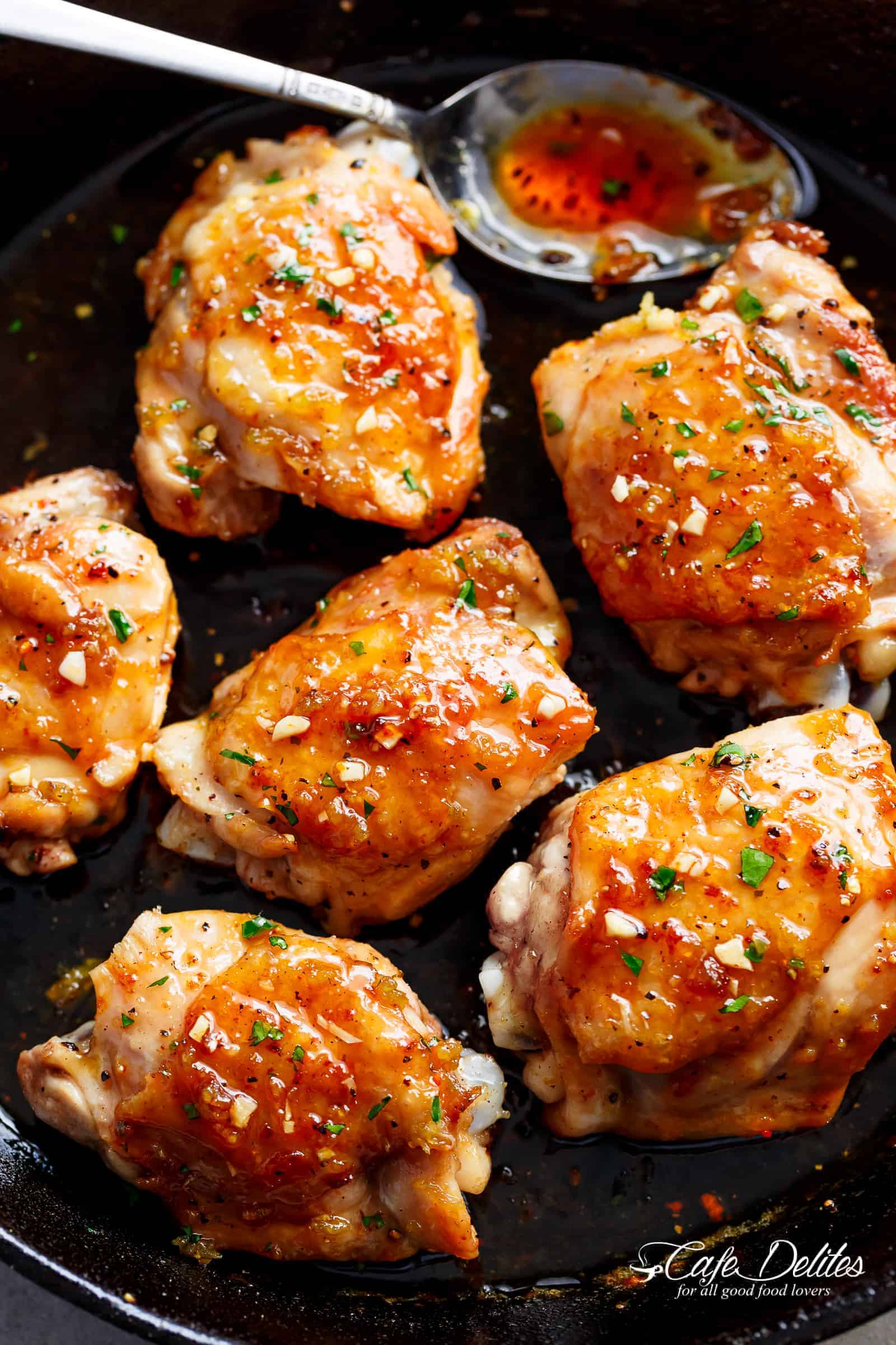 Honey Garlic Chicken thighs with a sticky sauce and fresh herbs sprinkled on top in a pan. 