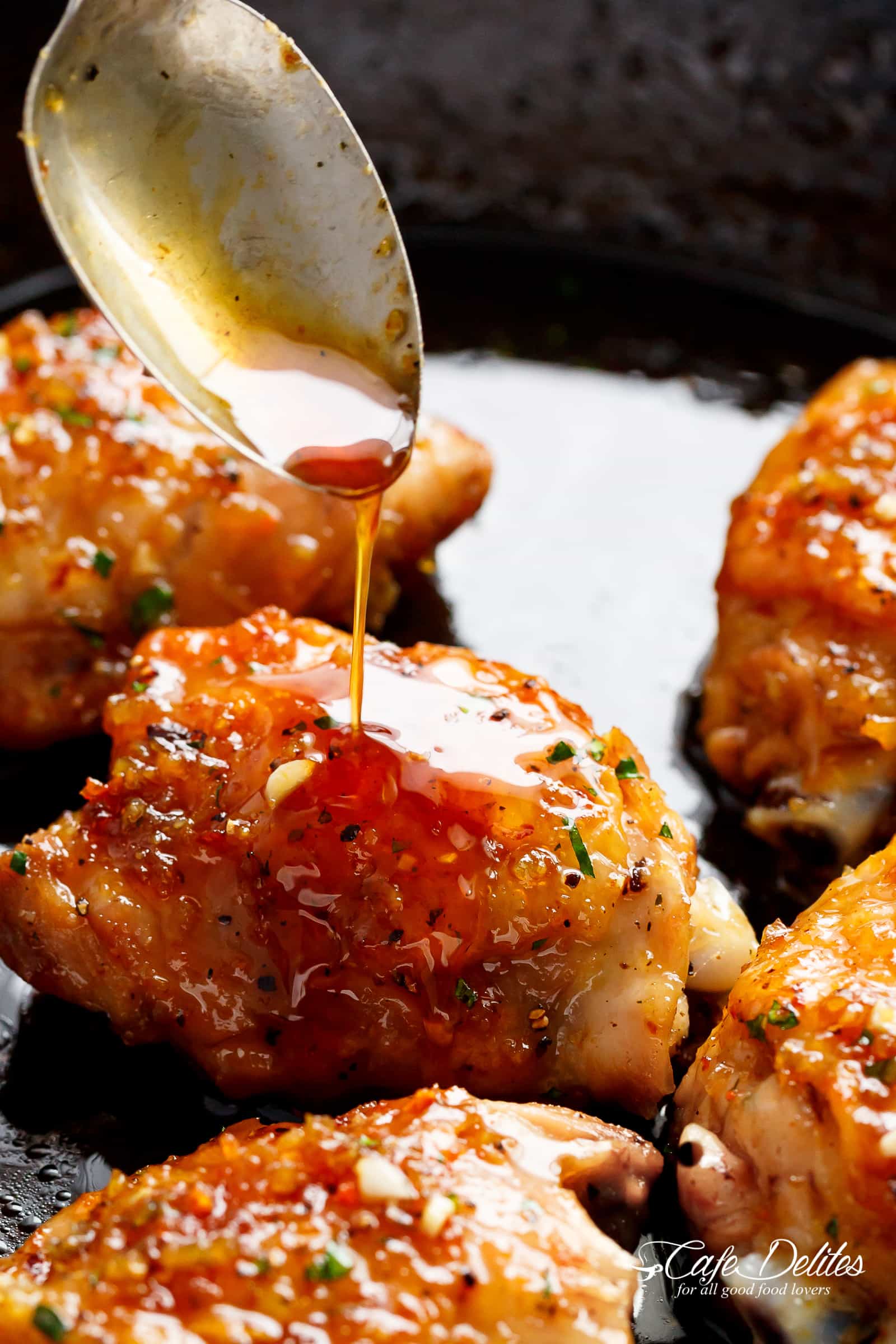 A silver spoon pouring sauce onto a crispy chicken thigh in a pan, looks delicious  