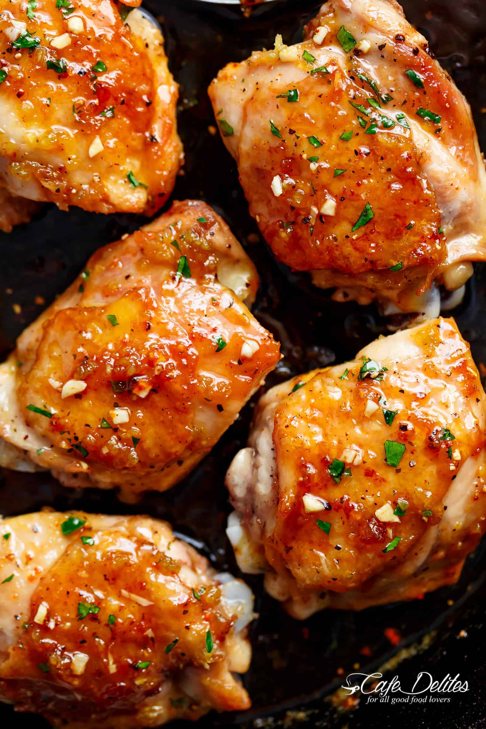 Chicken pieces glazed in honey garlic sauce in a pan, with chopped, fresh herbs on top. 