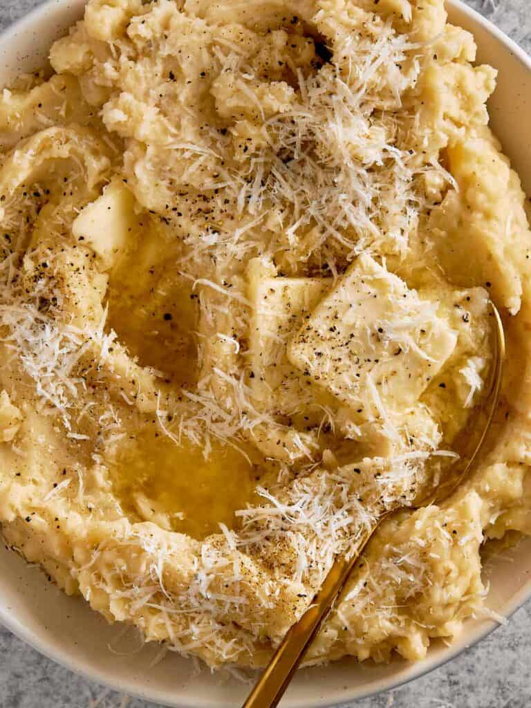 top down view of a white bowl filled with creamy potatoes and two cubes of butter with herbs on top close up shot