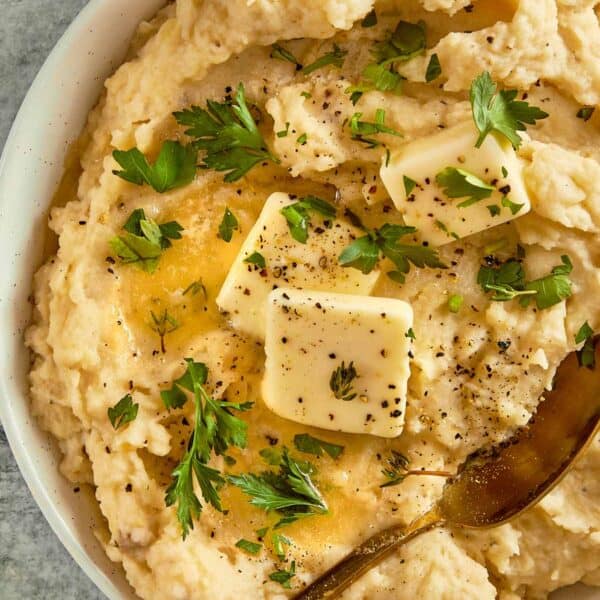 top down view of a white bowl filled with creamy potatoes and two cubes of butter with herbs on top close up shot with chives on top