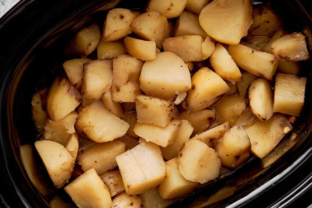 a top down view of cut up baby potatoes inside a slow cooker