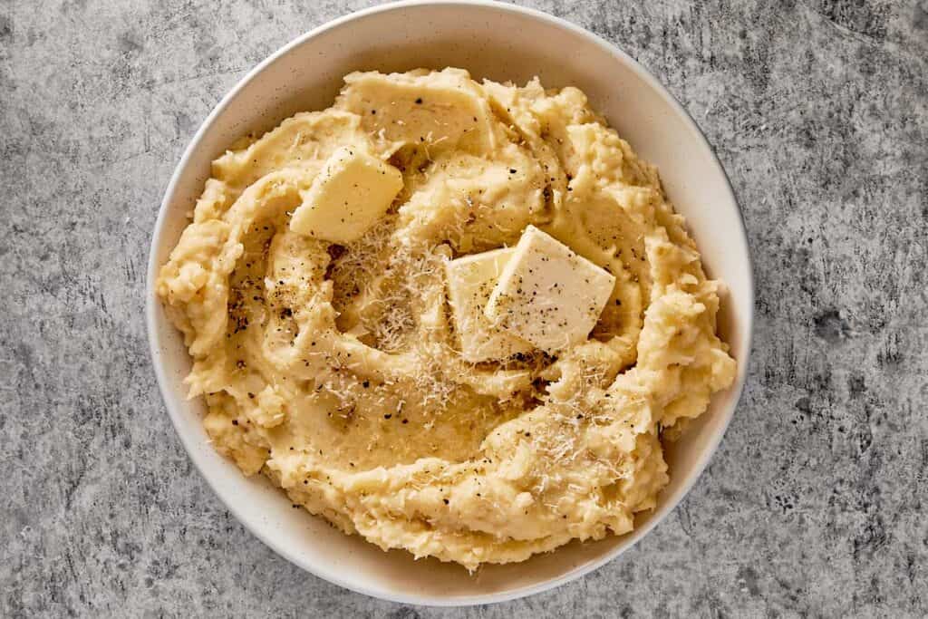 top down view of a white bowl filled with creamy potatoes and two cubes of butter with herbs on top
