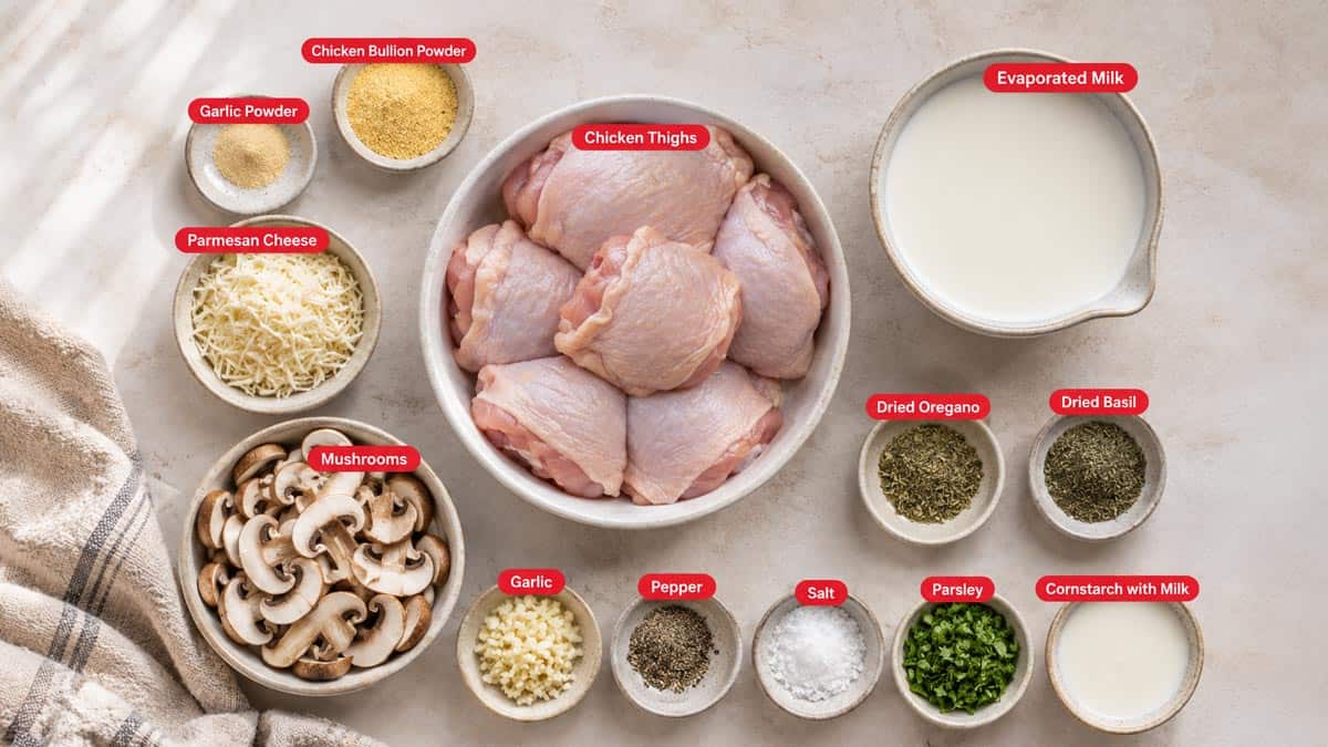Top shot of ingredients: Chicken bullion powder, chicken thighs, evaporated milk, parmesan cheese, mushrooms, garlic, pepper, salt, parsley, garlic powder, dried oregano, dried basil, and cornstarch with milk.