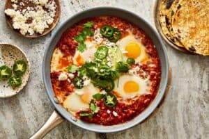 a top down view of a pan with two cooked eggs and tomato and jalapenos