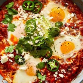 a top down view of a close up of a tomato and egg mixture with green jalapenos