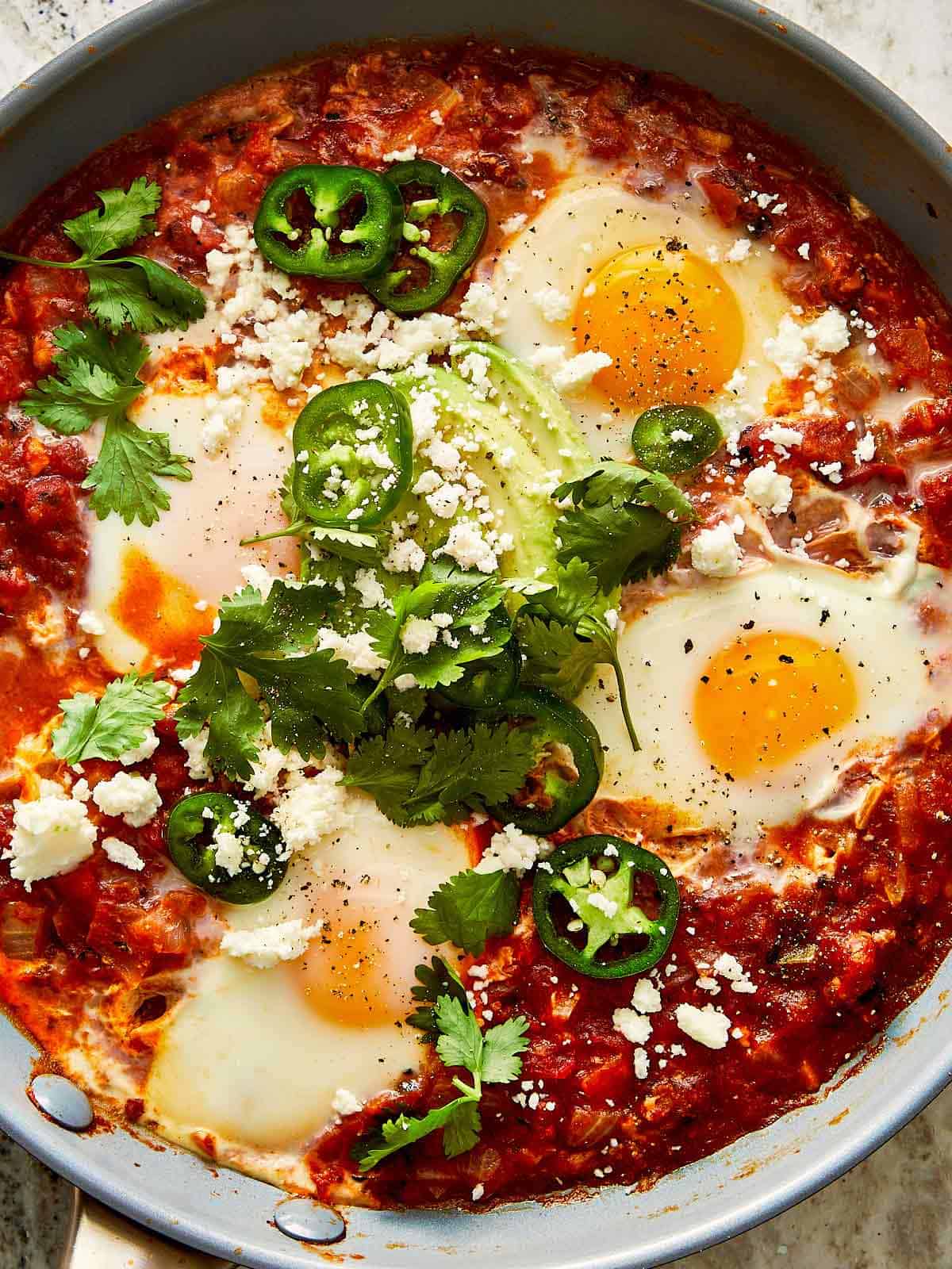 a top down view of a close up of a tomato and egg mixture with green jalapenos