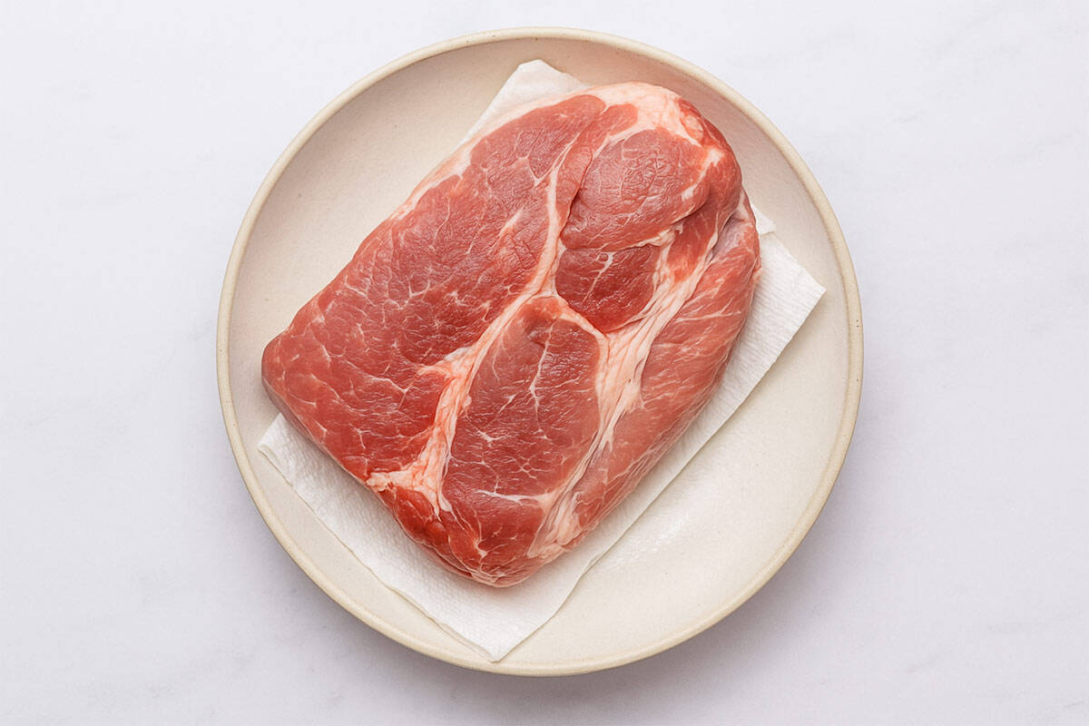 Raw boneless pork butt placed on a round white plate, resting on paper towels, ready to be seasoned.
