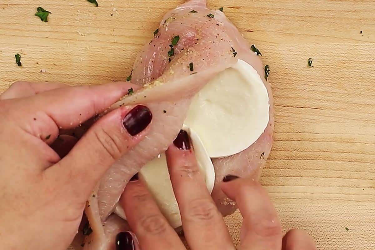 Placing two slices of mozzarella inside the pocket of the chicken.
