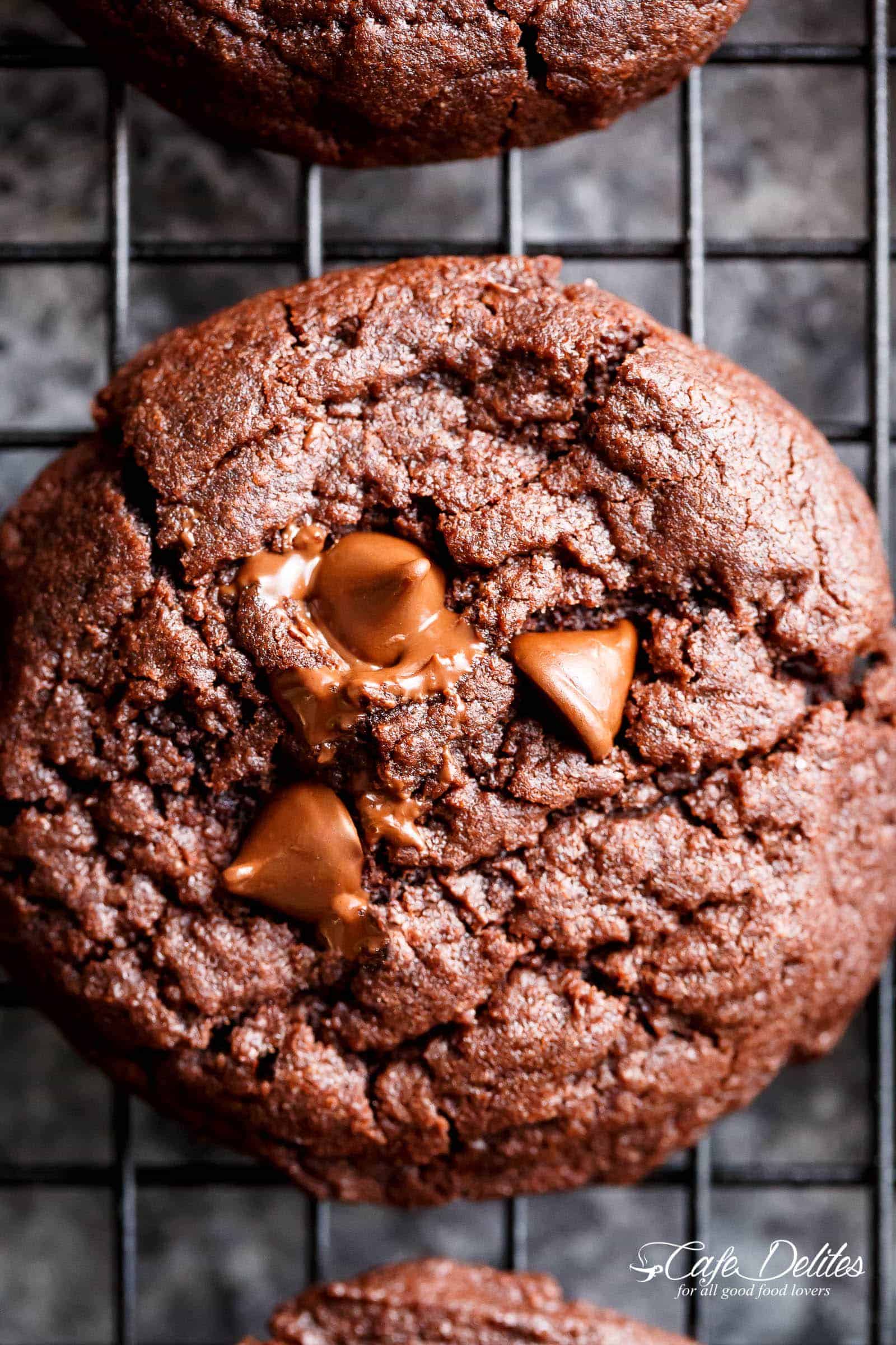 Close up of chocolate brownie cookie with meting chocolate chips on top resting on a cooling rack. 