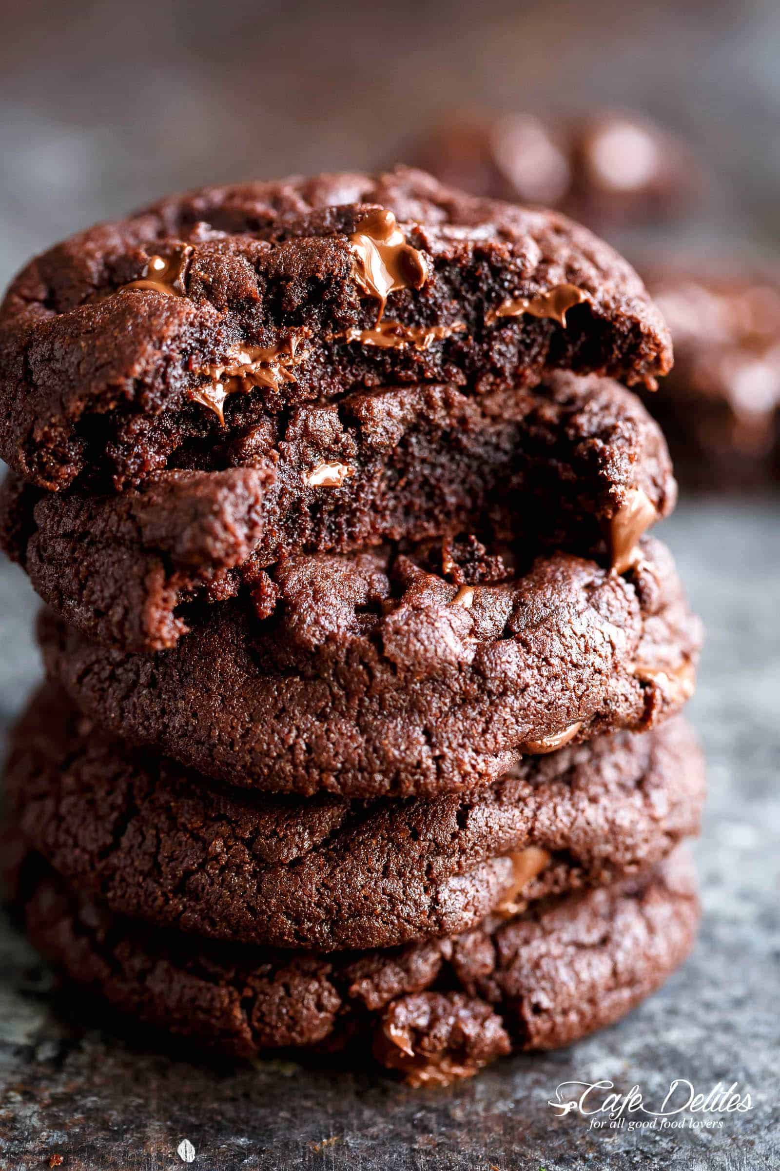 Stack of chocolate brownie cookies with bites taken out of the top two, exposing the gooey centre. 
