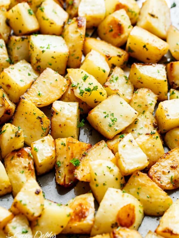Yummy Crispy garlic roasted potatoes sprinkled with fresh green herbs on a baking tray.