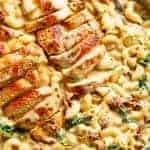 Tuscan chicken sliced, on top of a bed of creamy pasta with sundered tomatoes and spinach with Fresh herbs sprinkled on top.