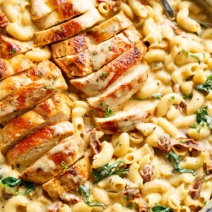 Tuscan chicken sliced, on top of a bed of creamy pasta with sundered tomatoes and spinach with Fresh herbs sprinkled on top.