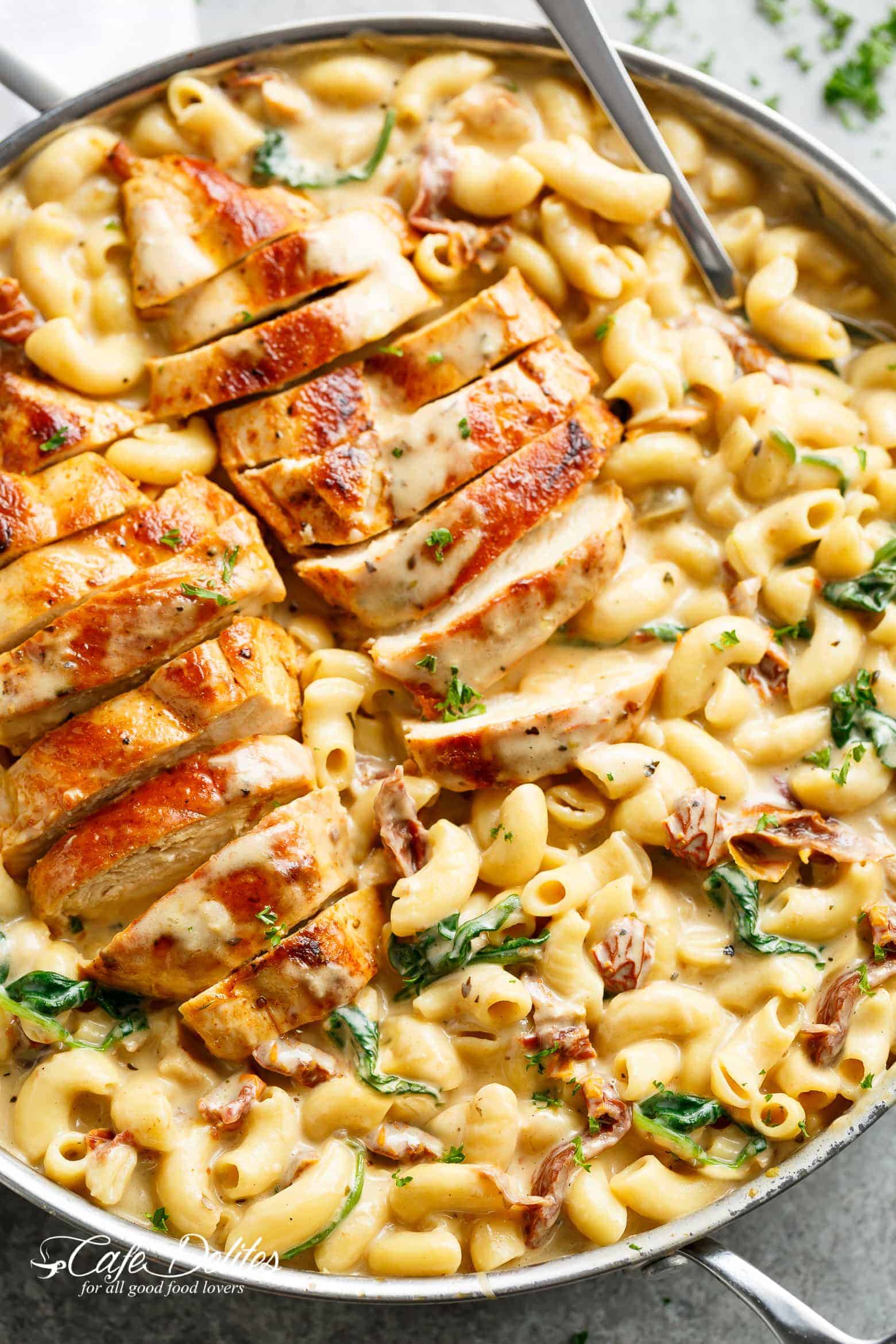 Tuscan chicken sliced, on top of a bed of creamy pasta with sundered tomatoes and spinach with Fresh herbs sprinkled on top.