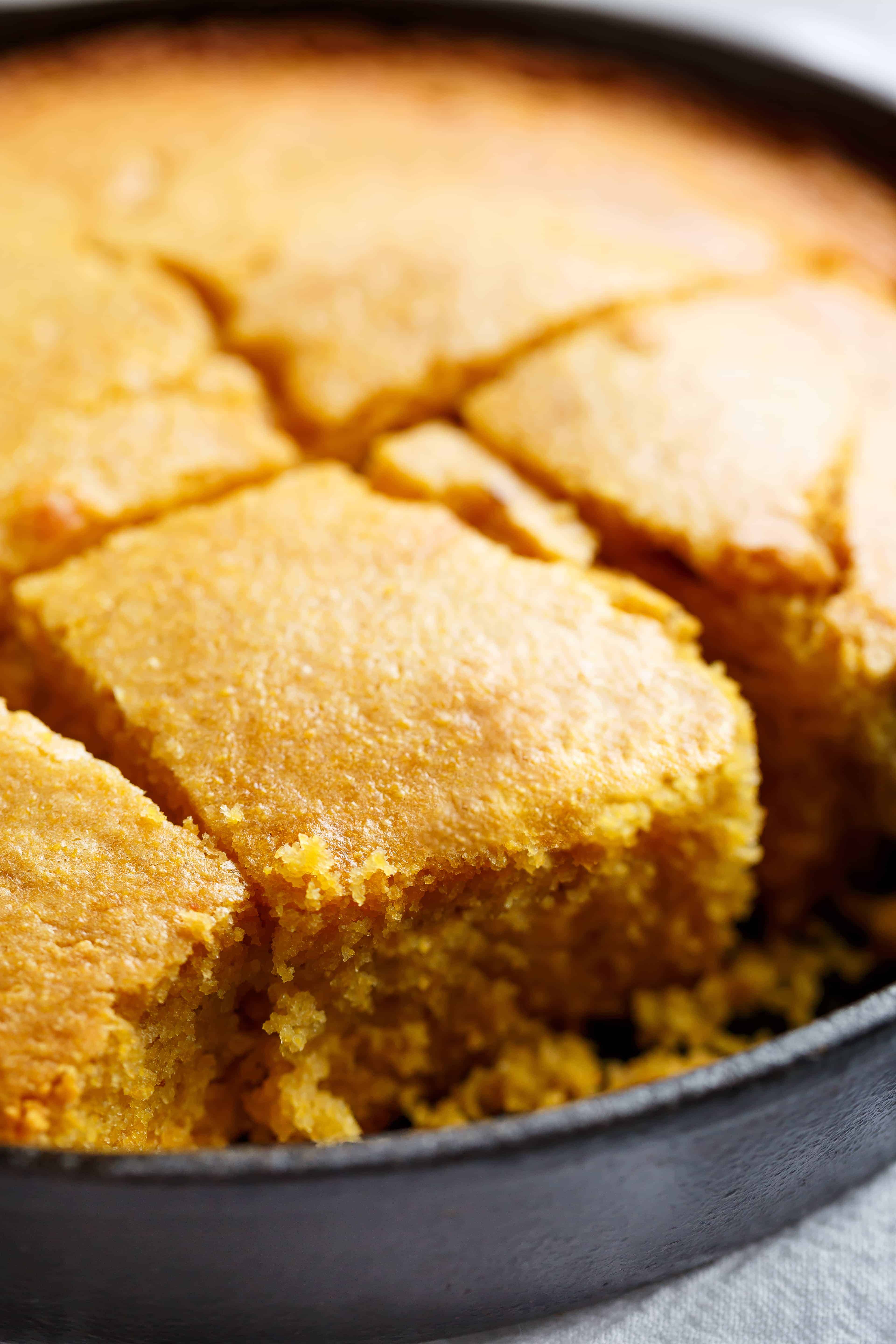 Side view of Buttermilk cornbread in a skillet cut into showing the fluffy yellow inside.