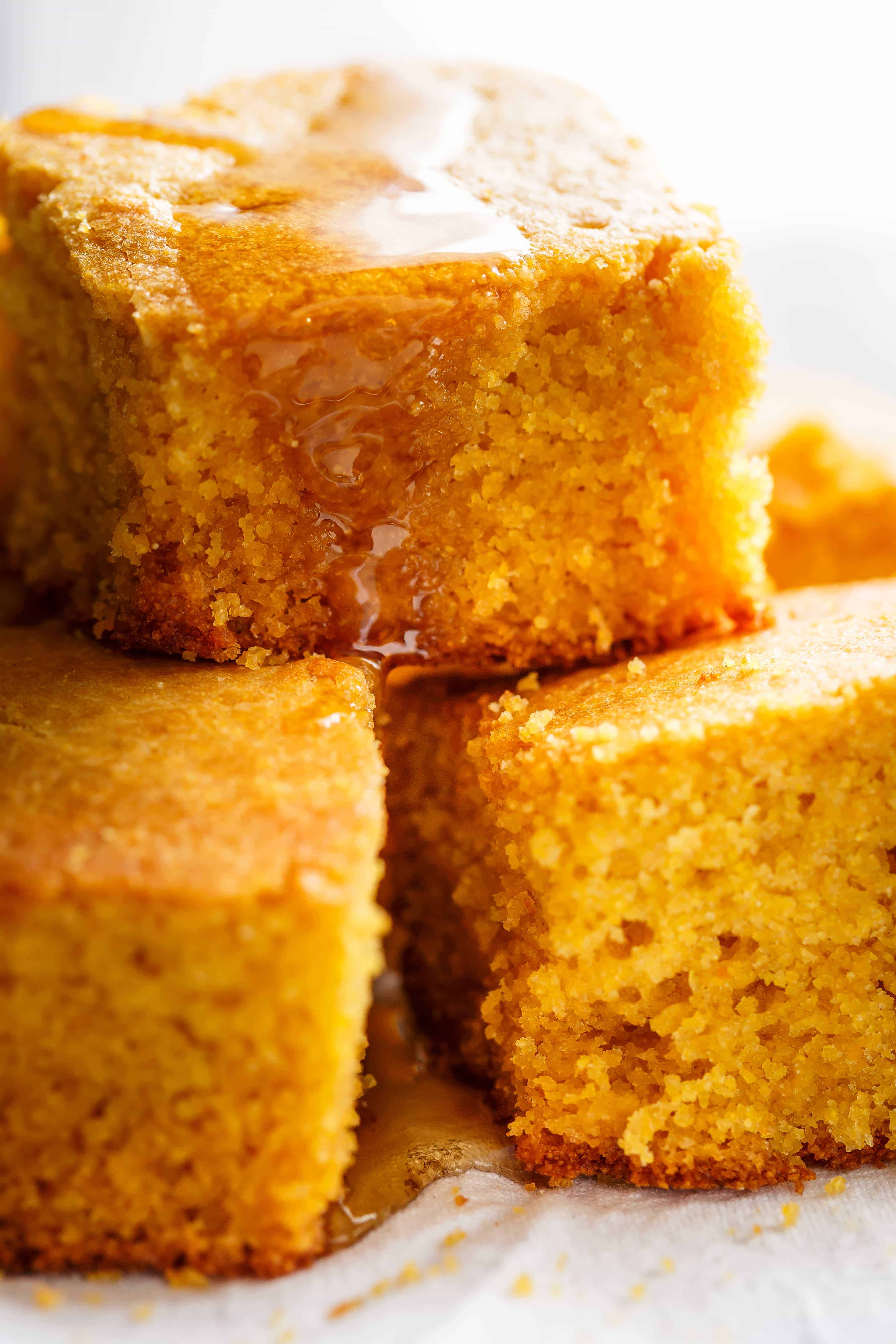 Close up image of moist buttermilk cornbread slices stacked and drizzled with syrup.