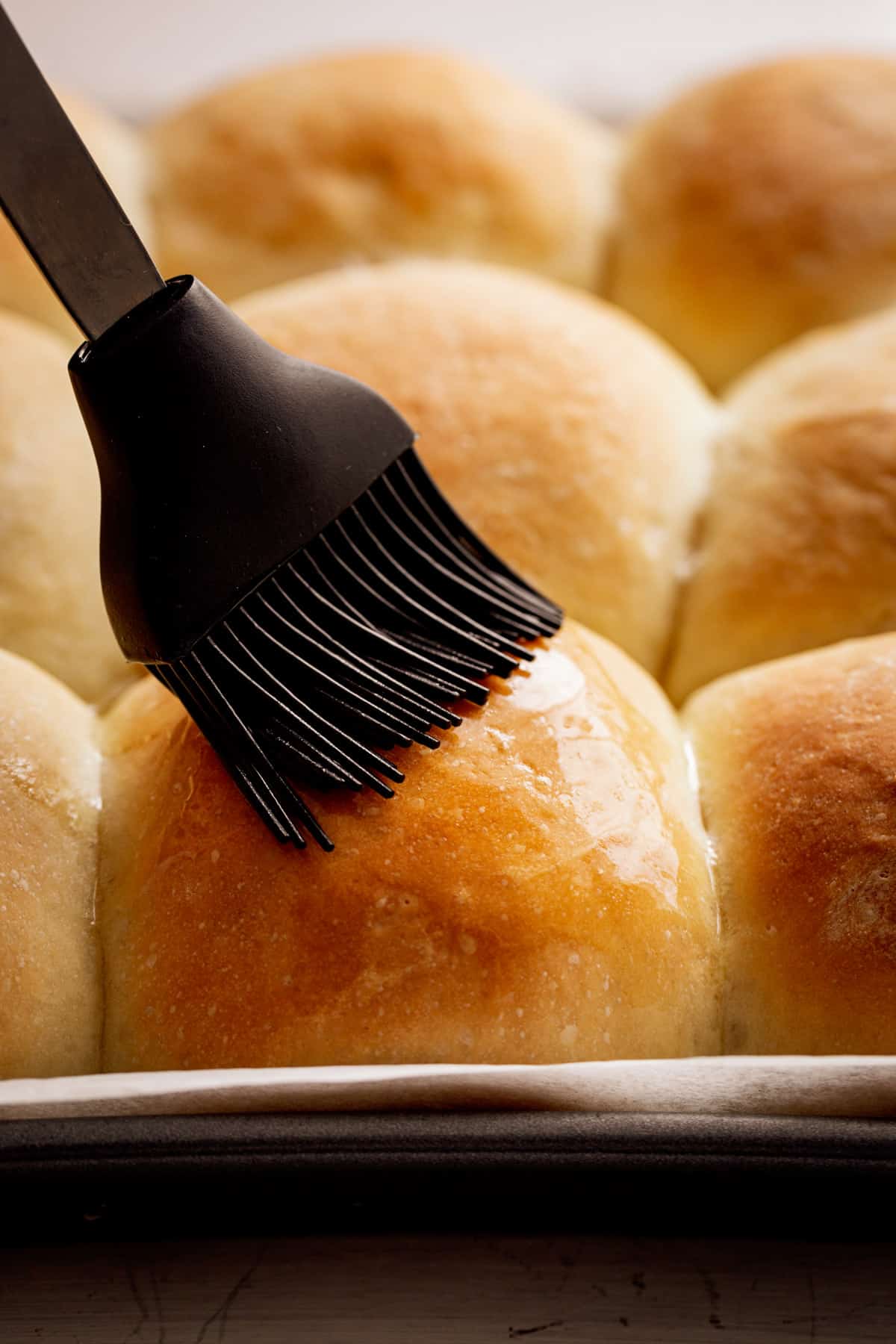 Golden soft dinner rolls being glazed with melted butter.